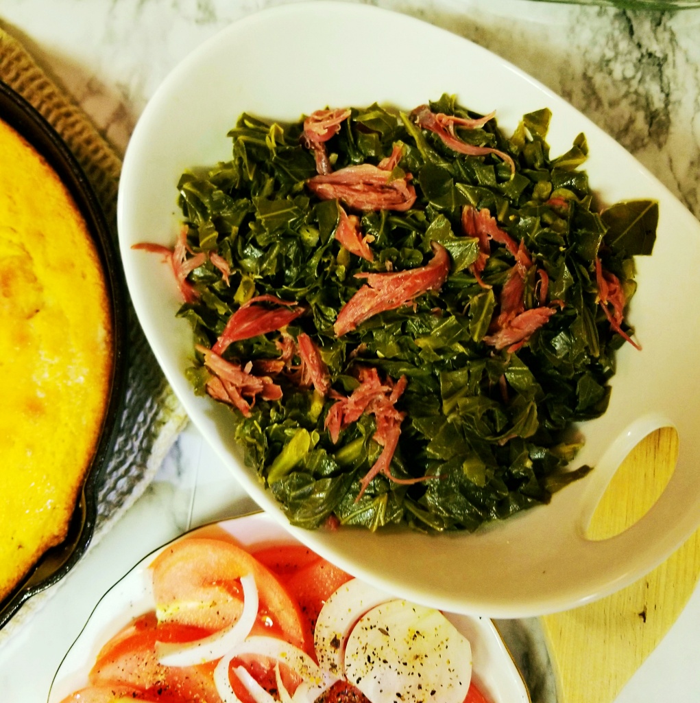 Collard Greens in a serving bowl with cornbread and tomatoes. 